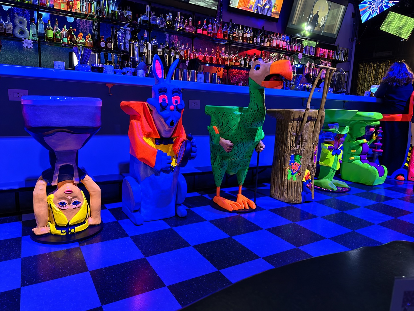 The Rabbit Hole’s sculpted character stools and checkerboard floor under blue lighting